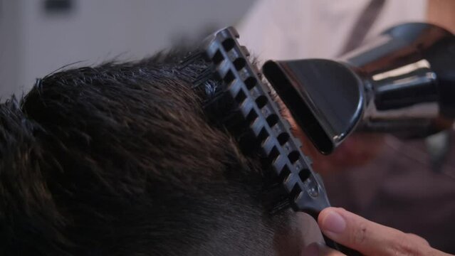 Black hair dryer and black comb driven through top of head with black hair, filmed as closeup shot in slow motion handheld style