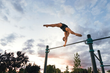 young man doing one hand handstand on a bar in a calisthenic park