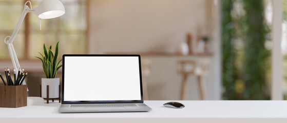 A minimalist workspace with a white-screen laptop computer and accessories on a white table indoors.