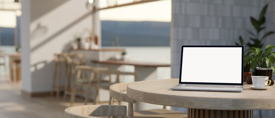 A white-screen laptop computer mockup on a table in a modern, Scandinavian cafe.