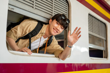 A happy Asian man is on a train, smiling and waving his hand, and traveling somewhere by a train.