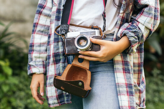Unrecognizable woman taking photos with analog camera in the field at sunset