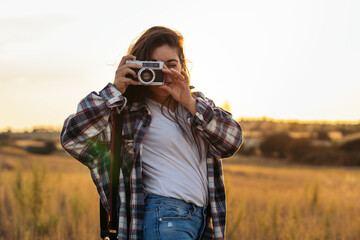Young woman taking photos with analog camera in the field at sunset