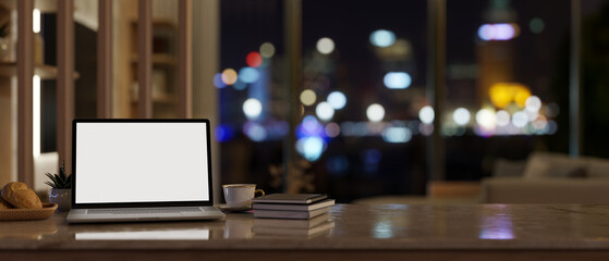 Home workspace at night with a laptop mockup and accessories on tabletop in a modern living room.
