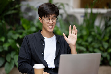 A positive Asian man working remotely at a coffee shop, having an online meeting with his team.