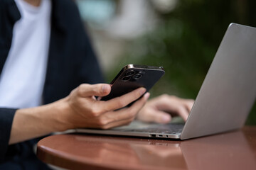 Cropped image of a Asian man using his smartphone and laptop while working remotely in a coffee shop