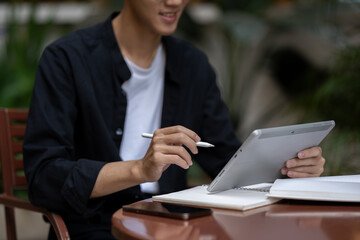 Cropped image of an Asian man is working on his tablet at an outdoors table at the coffee shop.