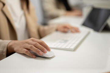 Close-up hand image of a businesswoman working at her desk in the office, using a wireless mouse.