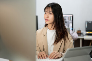 A focused Asian businesswoman is working on her tasks on her computer in the office.