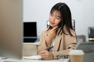 A young, beautiful Asian businesswoman is busy with her work in the office, talking on the phone.