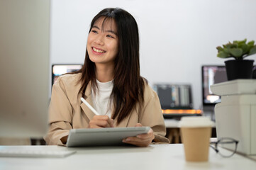 Attractive Asian businesswoman is working at her desk in the office, using her digital tablet.