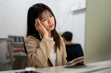 A tired and overworked Asian businesswoman is working on her project on computer in the office.
