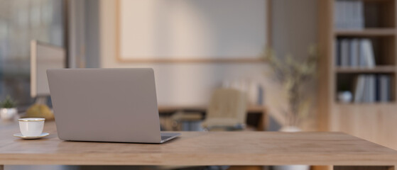 Back view image of a laptop computer on a wooden table in a modern, minimal office.