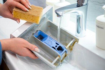 Housewife hands cleaning plastic container of washing machine use sponge and water at bathroom sink