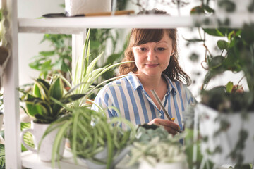 A young woman enjoys caring for flowers. Watering indoor plants and admiring them.