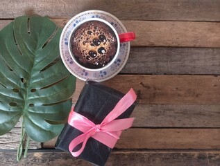 Coffee, give box and monstera leaf on wood background 