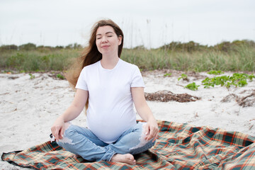 Fototapeta na wymiar Caucasian pregnant woman meditating at the beach. Happy pregnant woman connecting with nature. 