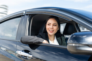 Young beautiful asian business women in suit getting new car. She very happy and excited. Smiling female driving vehicle on the road on a bright day.