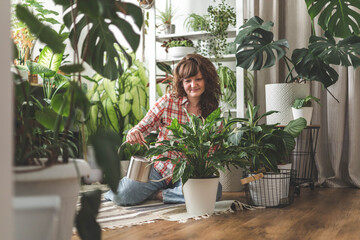 A young woman enjoys caring for flowers. Watering indoor plants and admiring them.