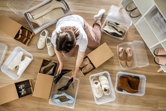 Woman arrangement shoes into plastic container and cardboard box seasonal storage organizing closeup