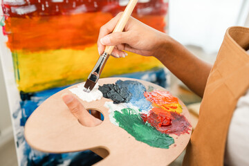 Close up hand Asian woman artist working on painting with brush and variant acrylic color. Female artist painter on canvas in creative studio as art concept