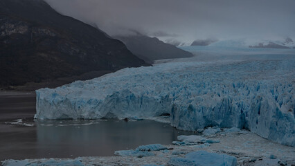 A beautiful glacier stretches between the mountains to the horizon. A mass of blue ice with cracks, crevices, sharp peaks. Thawed ice floes, icebergs floating in the lake. El Calafate. Perito Moreno