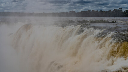 The famous Devil's Throat Waterfall. Close-up. Streams of water descend from the ledge of the river into the abyss. Spray, foam, fog. Clouds in the sky. Iguazu Falls. Argentina