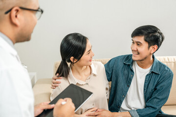 Fototapeta premium Asian family discussing fertility with a pediatrician. Young couple patients in fertility clinic consulting about IVF or IUI with doctor. Couple relationship therapy with a counselor