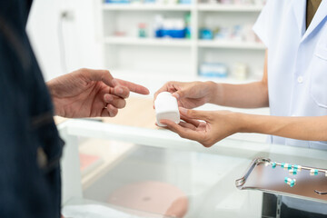 Pharmacist recommends medicines to customers.Taking the questions of medication. Asian female pharmacist giving prescription medications to customers at drugstore shelves.