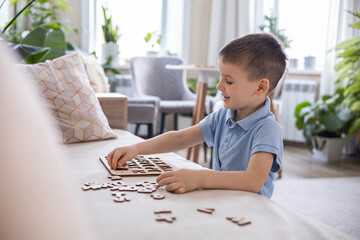 A Caucasian light-haired boy of five years old with blue eyes is putting together a puzzle 