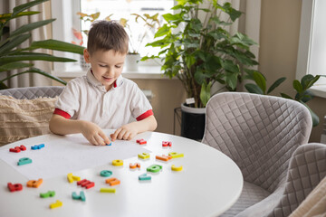 A Caucasian light-haired boy of five years old with blue eyes is putting together a puzzle 