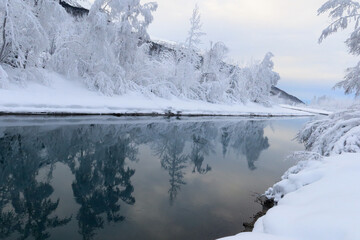 Snowy trees and mountains reflect in an Alaskan river.