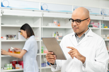 Professional asian man pharmacist checks inventory arrangement of medicine in pharmacy drugstore. Male Pharmacist wearing uniform standing near drugs shelves counter prescription to customers