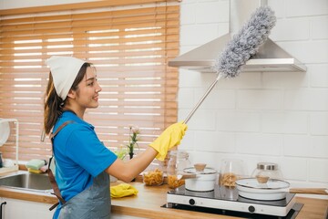 Asian maid in workwear and gloves cleans home dusts ventilation in kitchen. Hygiene emphasized...