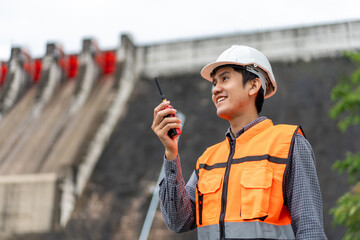 Obraz premium Professional asian maintenance engineer man with safety helmet in construction site dam with hydroelectric power plant and irrigation. Manager engineer man working at project big building.
