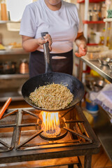 Chef using a pan sauteing noddles in a restaurant