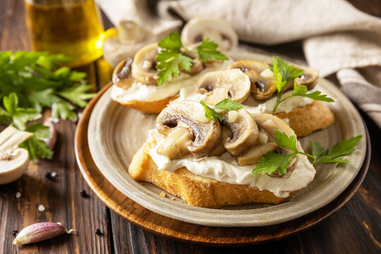 Toasted sandwich from baguettes bread with soft cheese and grilled mushrooms on wooden rustic  table. Homemade bruschetta with mushrooms.