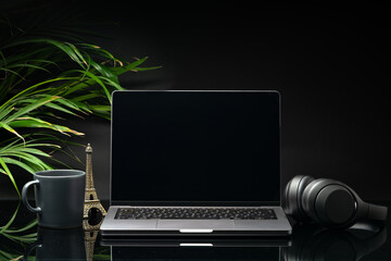 Laptop with black screen on working desk with cup and earphones on black background