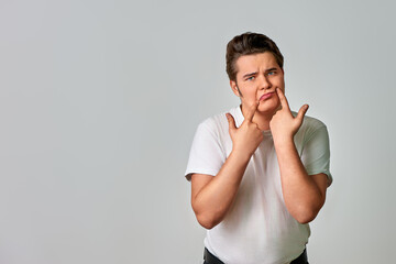 A man on a gray background shows a smile with his fingers