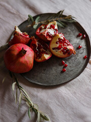 Image of Still Life with Turkish Pomegranate and olive branch on old retro plate. Dark wood background, antique copper plate. Fresh ripe whole pomegranates, opened pomegranate and seeds