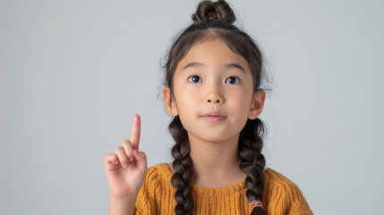 Beautiful Asian girl, pointing finger up at copy space isolated on background.