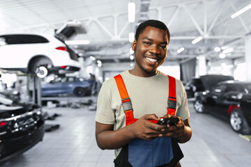 Young African mechanic man wearing uniform using mobile phone in a car service