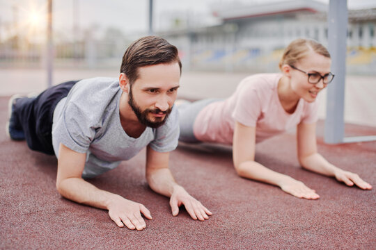 Couple sportsmen training together outdoor, plank pose on elbows