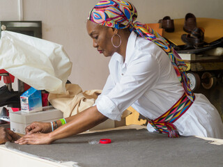 black african seamstress artisan tailor measure mark cut sew fabric on desk in the fashion workshop