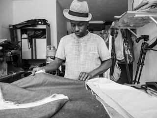 close up of african man tailor standing over a table with a cloth on it, preparing for a cut.