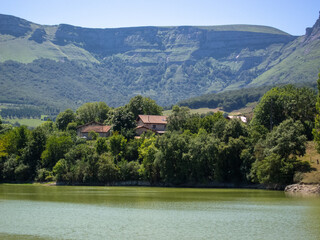 Fototapeta na wymiar Panoramic view of the natural area of the Maroño reservoir in Alava on a sunny day with a high water level surrounded by trees, vegetation and mountains, in the background a small house.