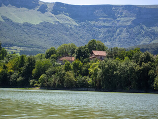 Panoramic view of the Maroño reservoir in Alava surrounded by many trees and vegetation and in the background some small rural style houses on a sunny day.