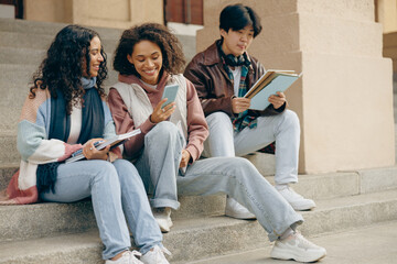 Group of young happy students watching something at mobile phone sitting on stairs