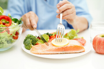 Asian elderly woman patient eating salmon stake and vegetable salad for healthy food in hospital.