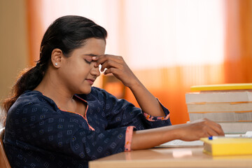 Fototapeta na wymiar Tiered young rubbing eyes while studying or reading book for examination at home - concept of education, quick nap and fatigue or exhausted.
